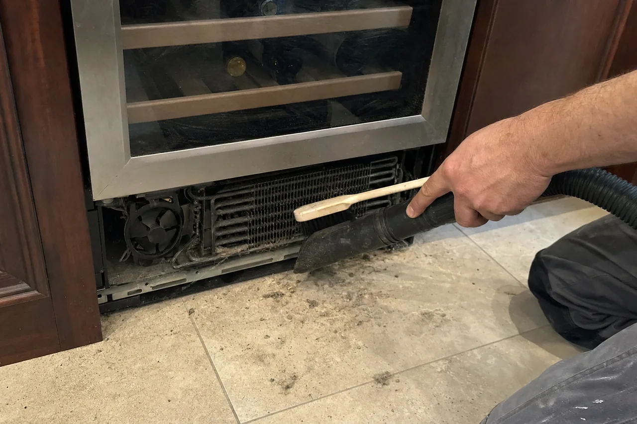 Floor-level frame of an appliance base panel removed in an older kitchen, tools and debris on the tiled floor