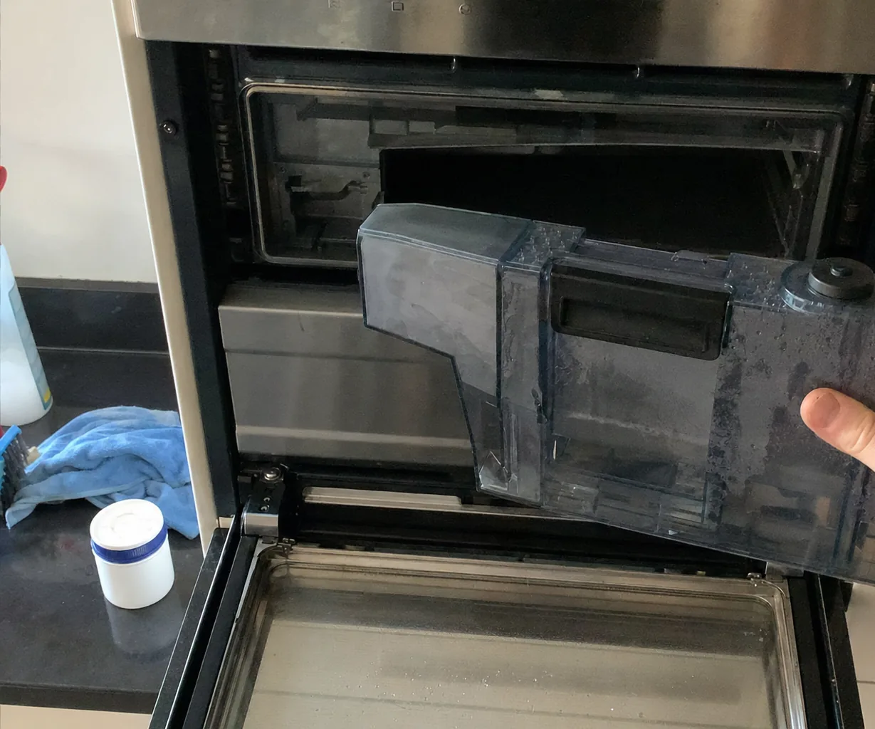 Right-hand crop of a water reservoir held up beside an open built-in oven cavity